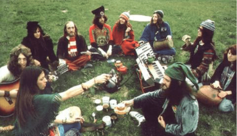 Group seated on grass playing music and sharing food in a picnic-like outdoor gathering