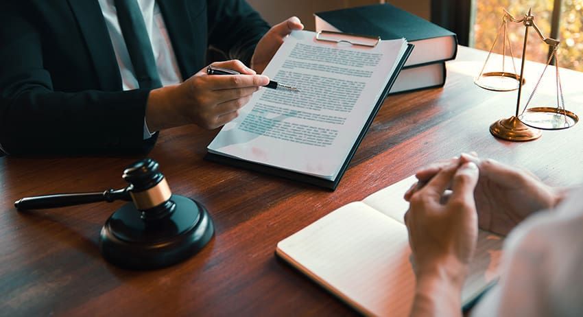 Lawyer reviewing documents at a desk with a gavel, open book, and writing hand nearby