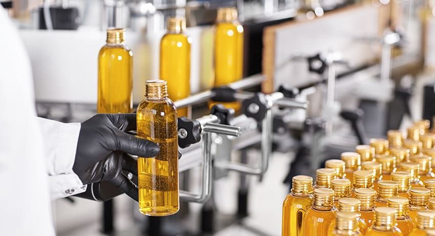 Gloved worker inspecting amber bottles on an assembly line in a bottling factory