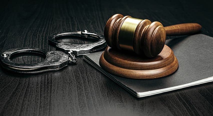 Judge’s gavel on a book beside handcuffs on a dark desk
