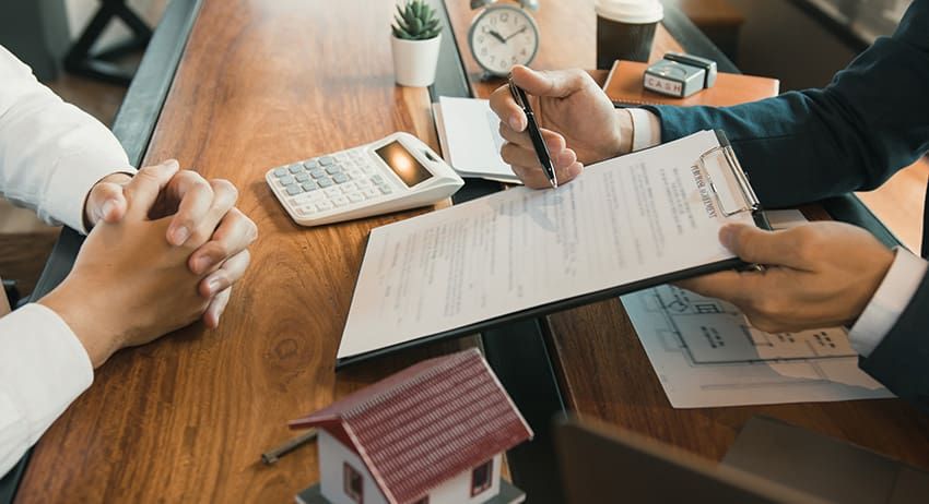 Hands reviewing documents at a wooden meeting table with calculator, pen, and small desk clock
