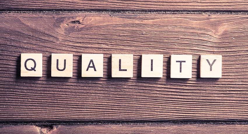 Wooden letter tiles spelling “QUALITY” on a rustic wood background.
