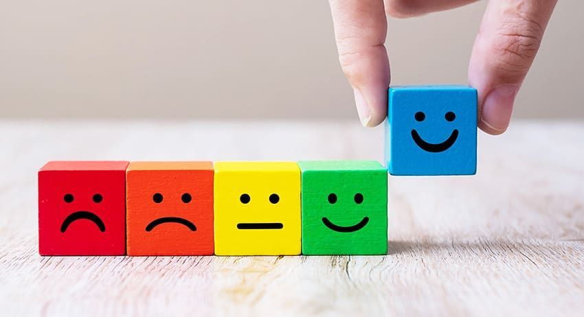 Hand placing blue smiling block beside row of colored blocks with different face expressions