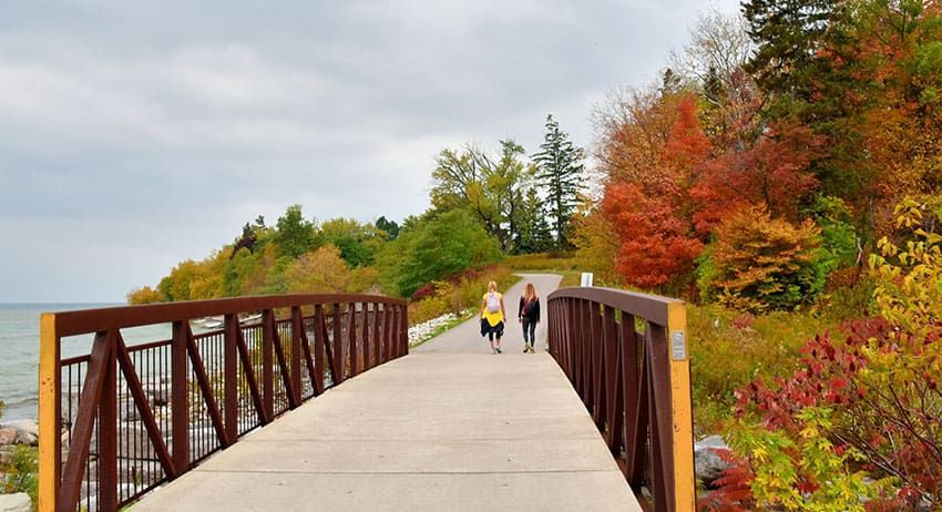 Pedestrian bridge over water with two people walking amid colorful autumn trees