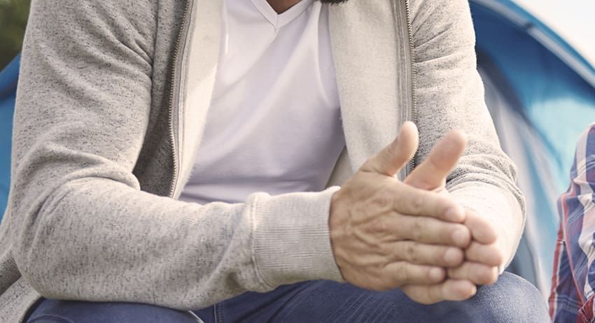 Person in gray sweater clasping hands while seated outdoors near a blue tent