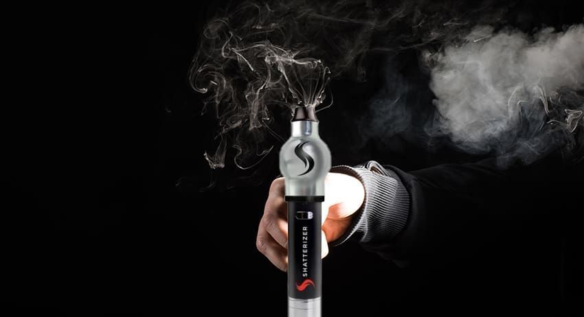 Hand holding a lit vape pen releasing smoke against a black background