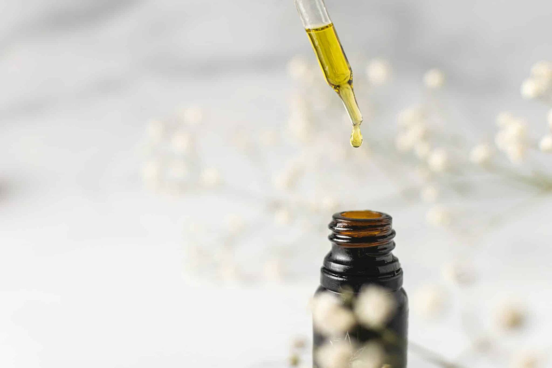 Dropper releasing yellow liquid into amber bottle with white capsules on a light background