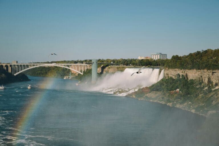 Rainbow over Niagara Falls with mist rising and a bridge in the distance