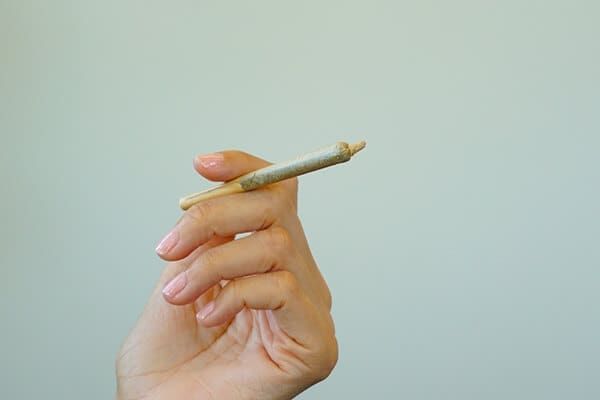 Hand holding a lit rolled cigarette against a plain light background