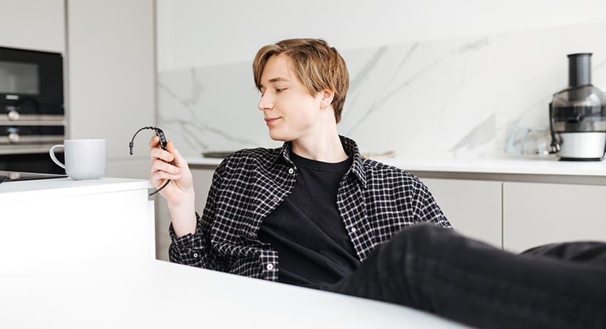 Person reclining in a bright kitchen, looking at a smartphone while holding a mug.