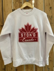 White sweatshirt with a red maple leaf and “STOK'D Canada” logo hanging on a wooden wall.