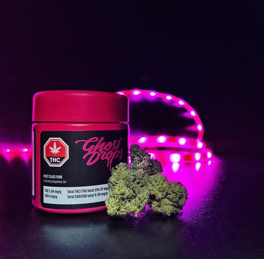 Magenta cannabis jar with green buds, lit by pink neon against a dark background