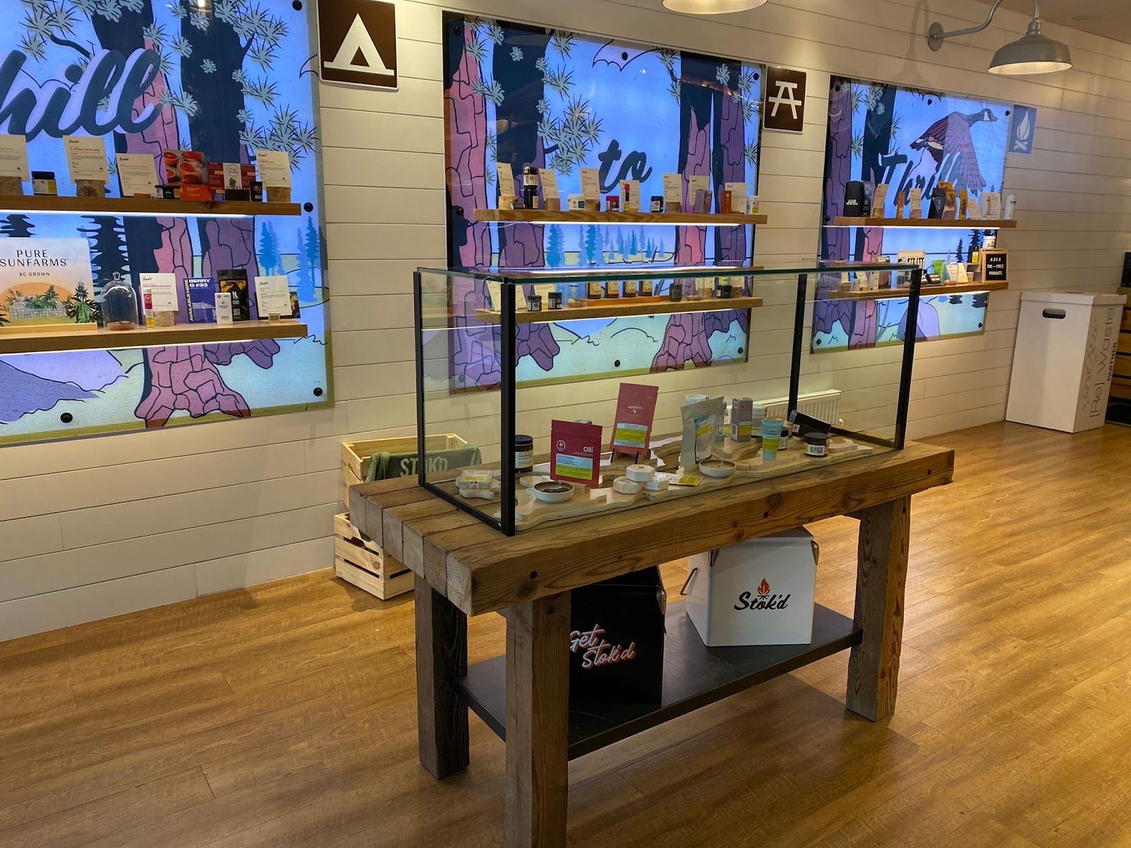 Glass display table in a bright retail store, with wall-mounted screens and a wooden floor.