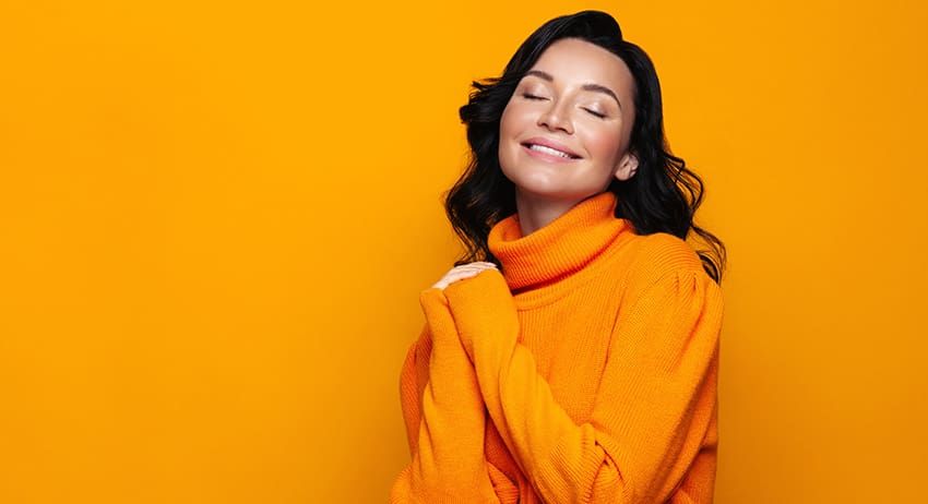 Smiling person in an orange sweater against a bright orange background