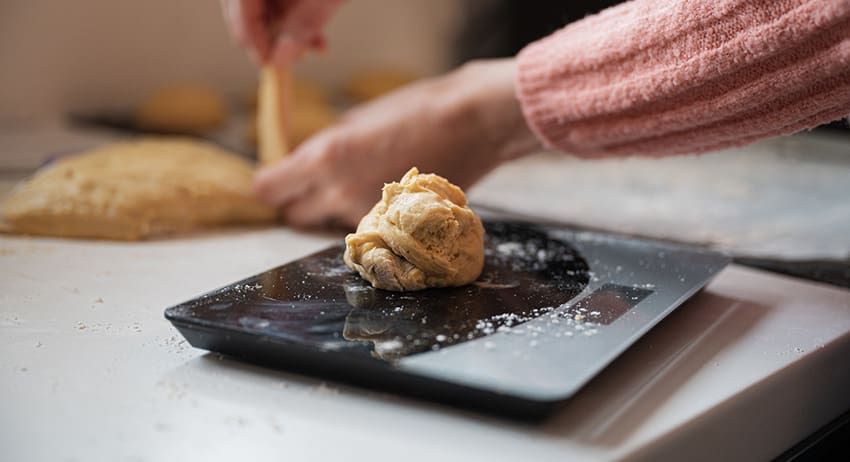Hand placing dough on a black plate with flour on a kitchen counter