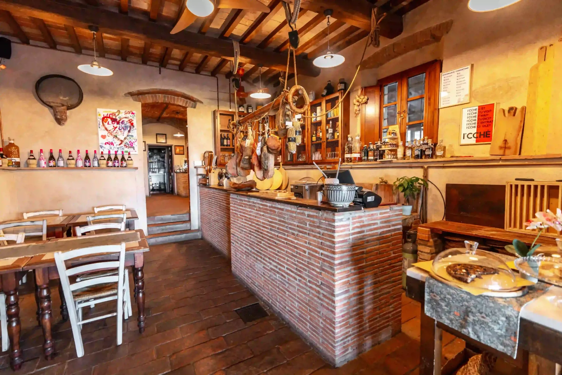 L'interno rustico di un ristorante è caratterizzato da un bancone in mattoni, tavoli e sedie in legno con luci soffuse.