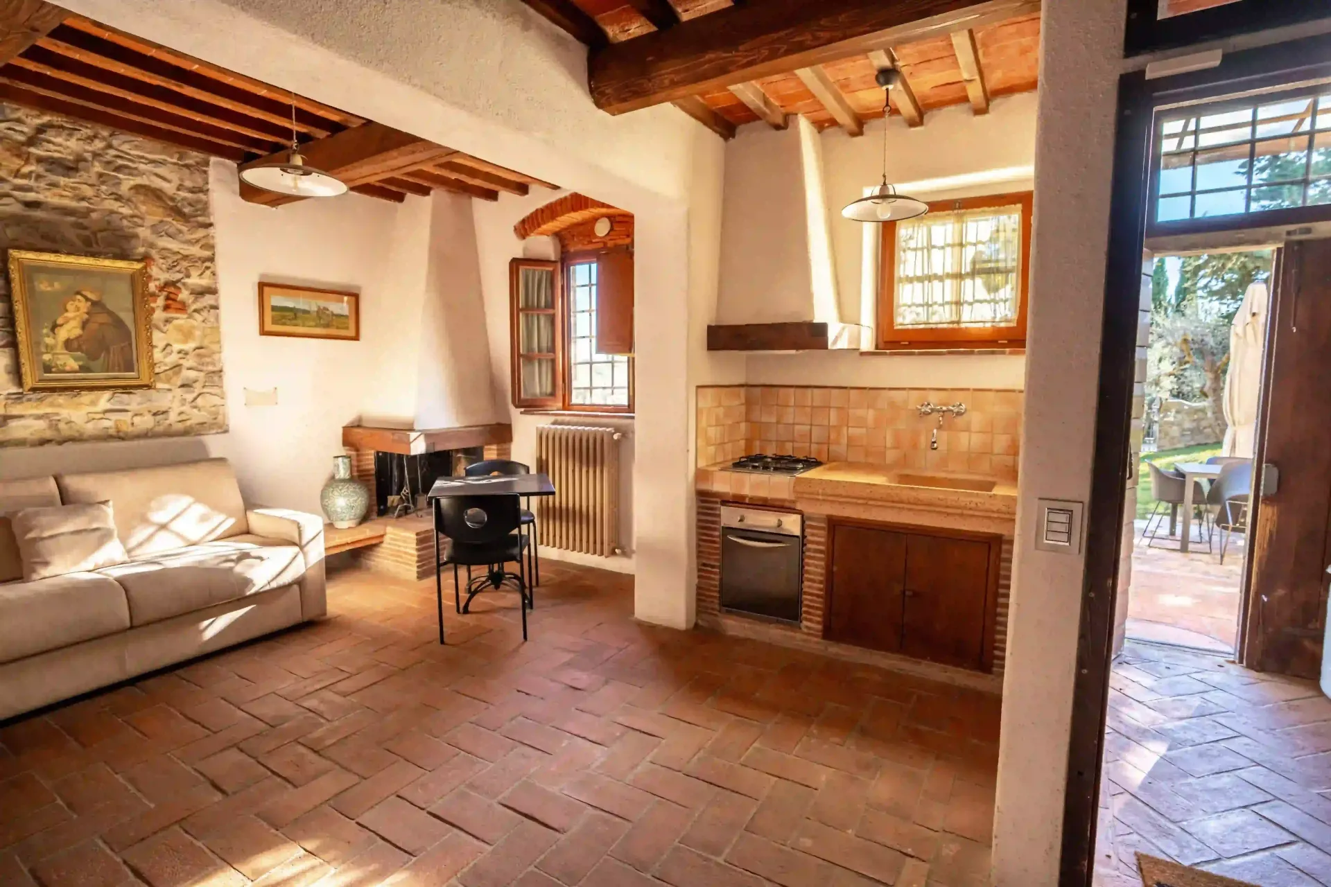 Un soggiorno rustico con pavimento in cotto, divano, tavolino da pranzo e cucina a vista con mobili in legno.