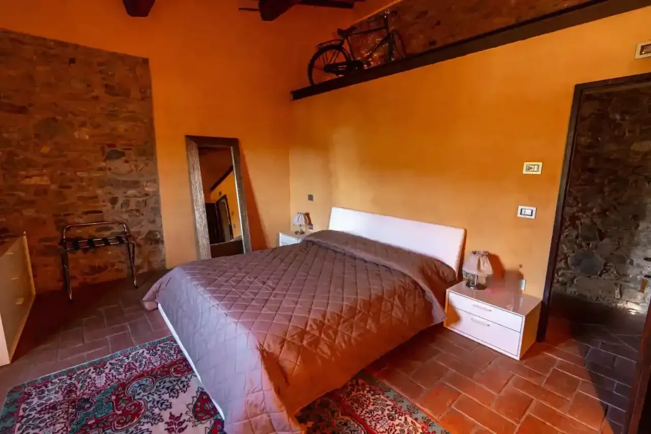 Una camera da letto con pareti arancioni, un muro di pietra, un letto con una coperta trapuntata marrone, uno specchio a figura intera e una bicicletta su una mensola.