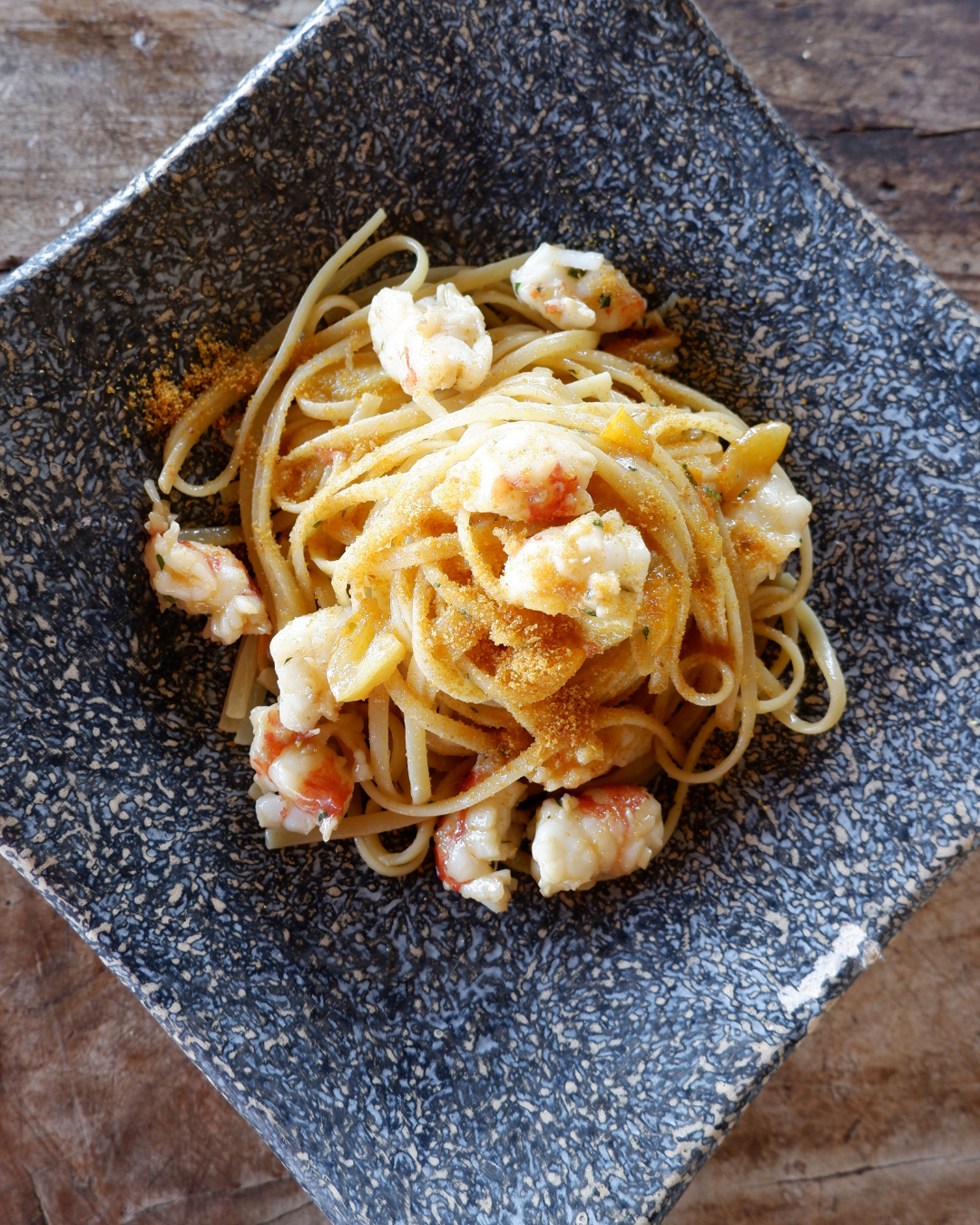 Un mucchio di pasta con un ricco ragù di carne, guarnito con un rametto di erbe aromatiche, servito in un'ampia ciotola nera.