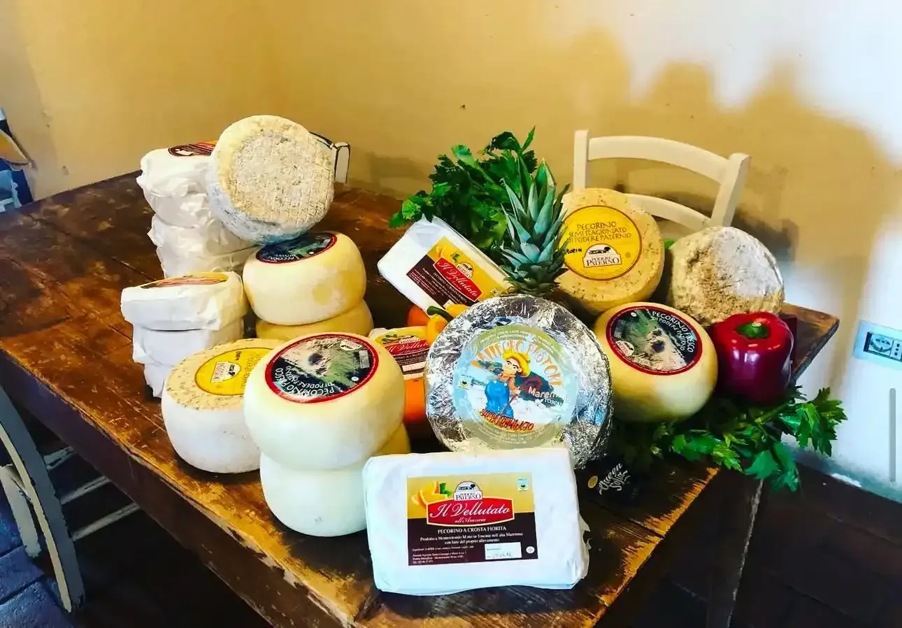 Un tavolo di legno carico di vari formaggi artigianali, rotondi e rettangolari, accompagnati da un ananas e un peperone.