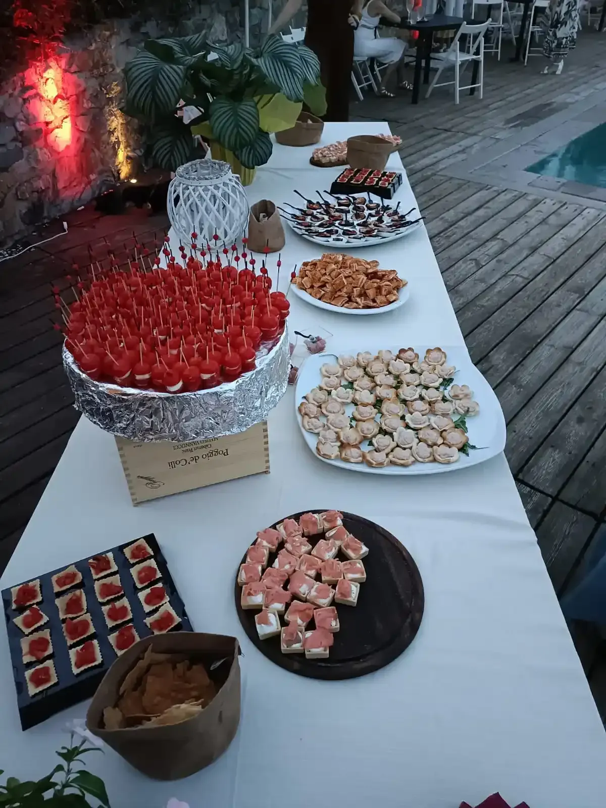 Un tavolo da buffet ricoperto da una tovaglia bianca offre una varietà di antipasti, tra cui spiedini rossi, cracker e stuzzichini.