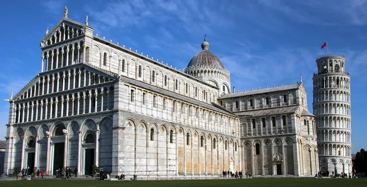 Il Duomo di Pisa, in marmo bianco, e l'iconica Torre Pendente si stagliano contro un cielo azzurro e limpido.