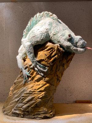 Eine weiße Tierskulptur, die über eine braune, felsartige Form drapiert ist, steht auf einem Tisch vor einer schlichten Wand.
