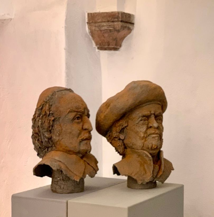 Zwei Tonbüsten auf Sockeln in einer Galerie, eine mit langen Haaren und eine mit Hut.