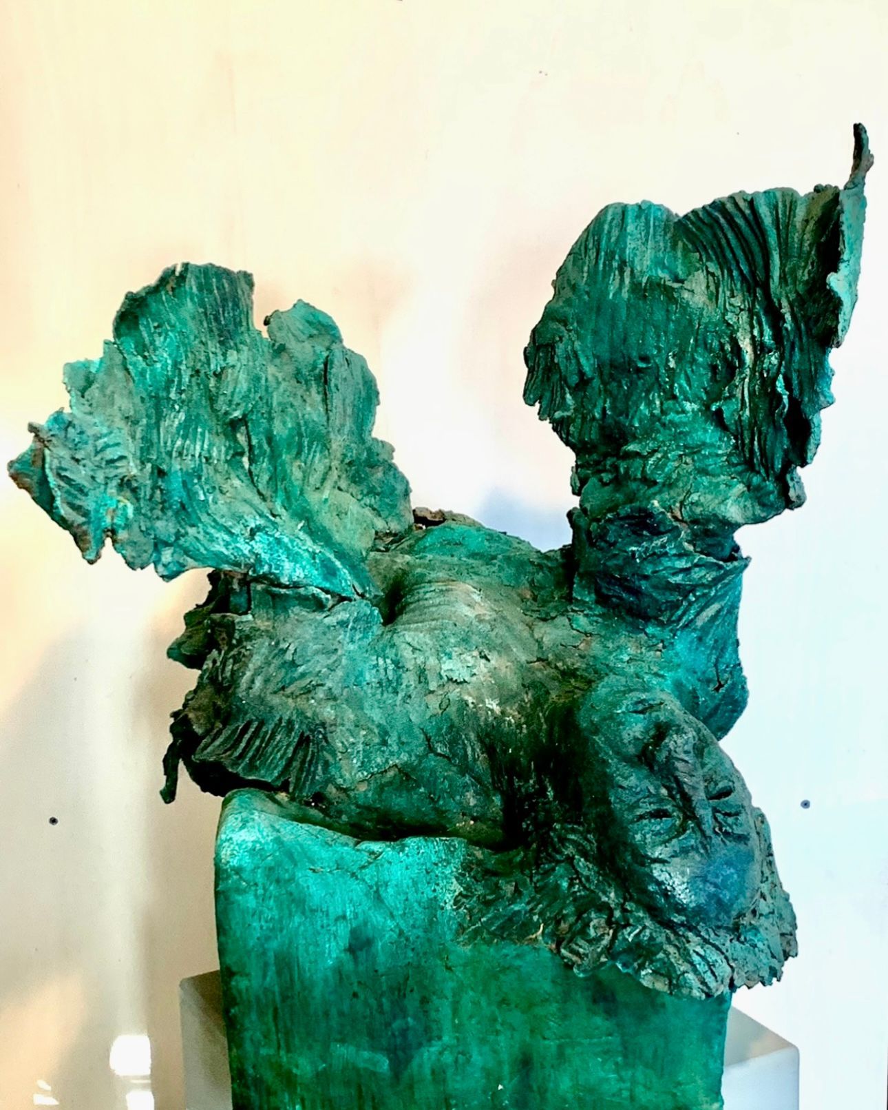 Abstrakte grüne Skulptur mit strukturierten, gewundenen Formen auf einem Sockel vor hellem Hintergrund