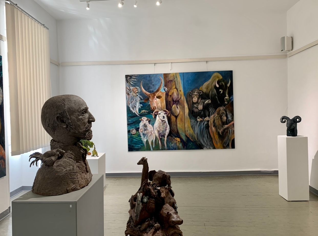 Kunstgalerie mit Skulpturen und einem farbenfrohen Tiergemälde an weißen Wänden.