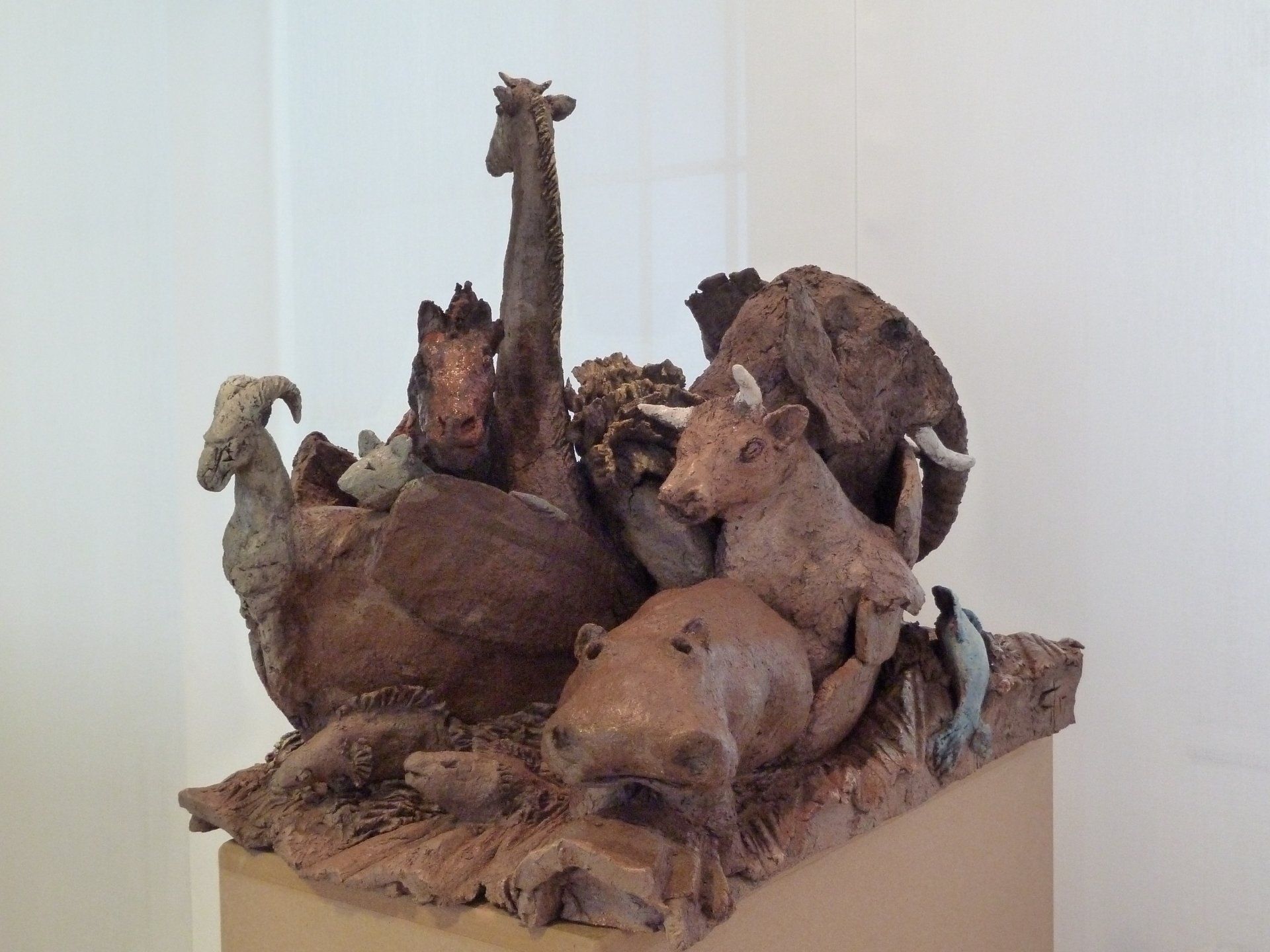 Rostbraune Tierskulpturen gruppierten sich auf einem Sockel in einem weißen Galerieraum.