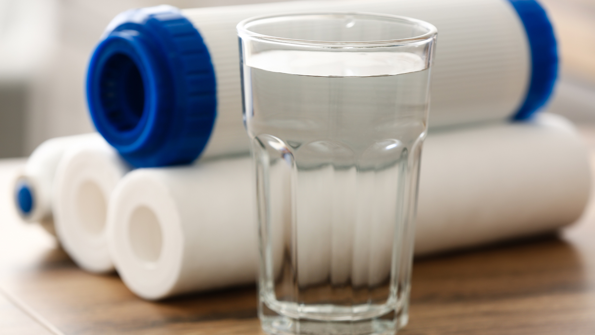 A glass of water is sitting on a wooden table next to a stack of water filters.