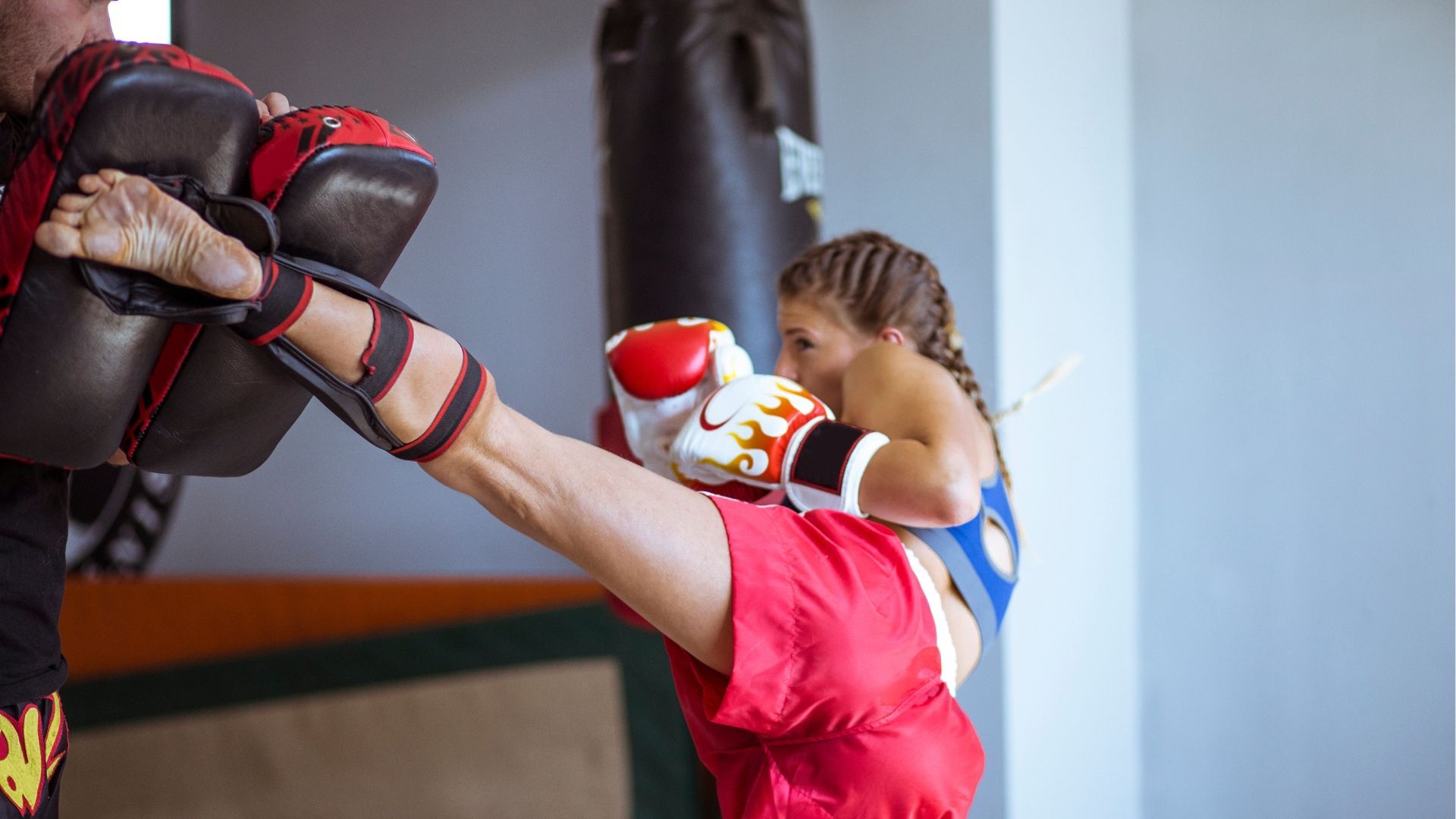 A woman at a Kickboxing Class executing a well-timed kick on a piece of equipment.