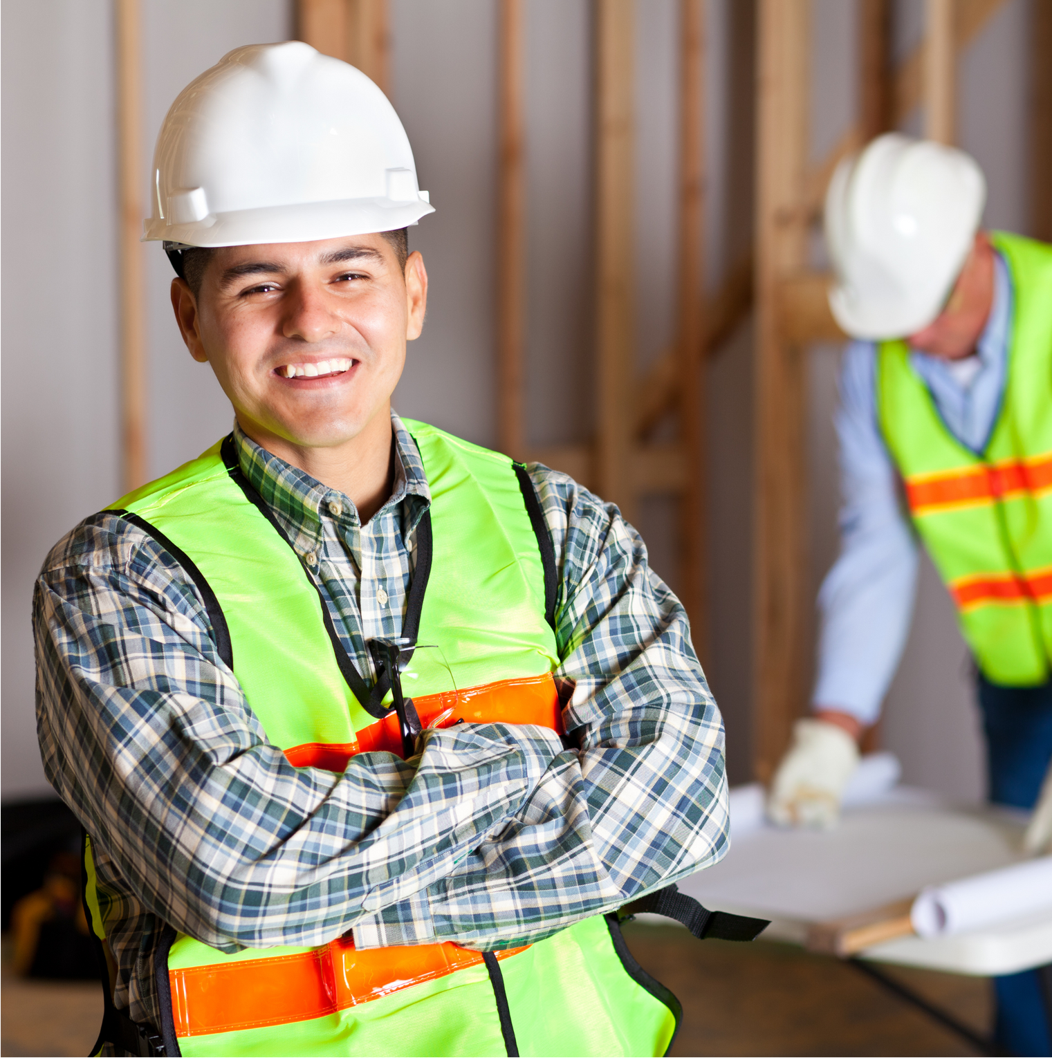 Apply Now A man wearing a hard hat and safety vest is smiling with his arms crossed