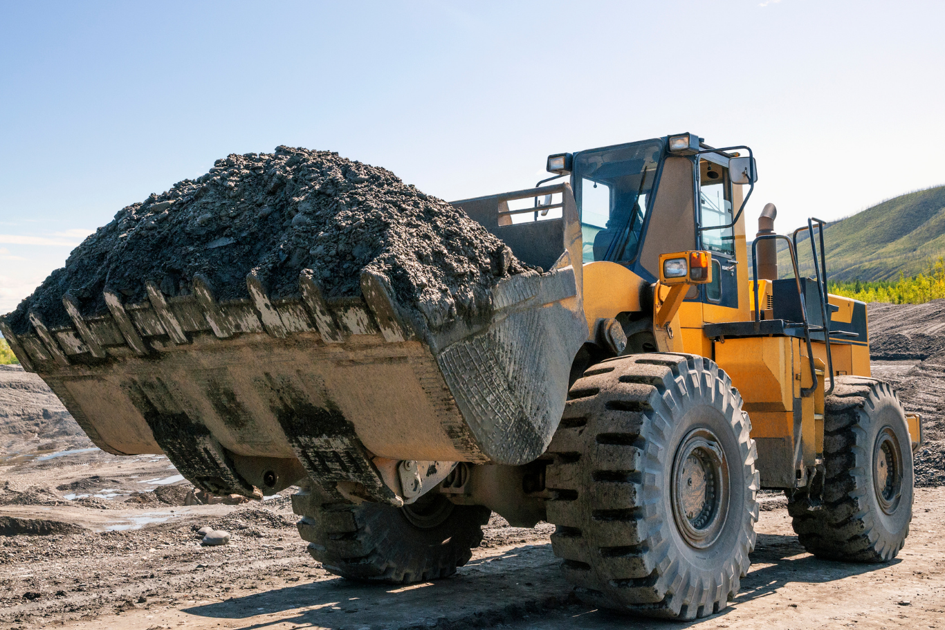 View All Services A bulldozer is carrying a large pile of dirt on a dirt road.
