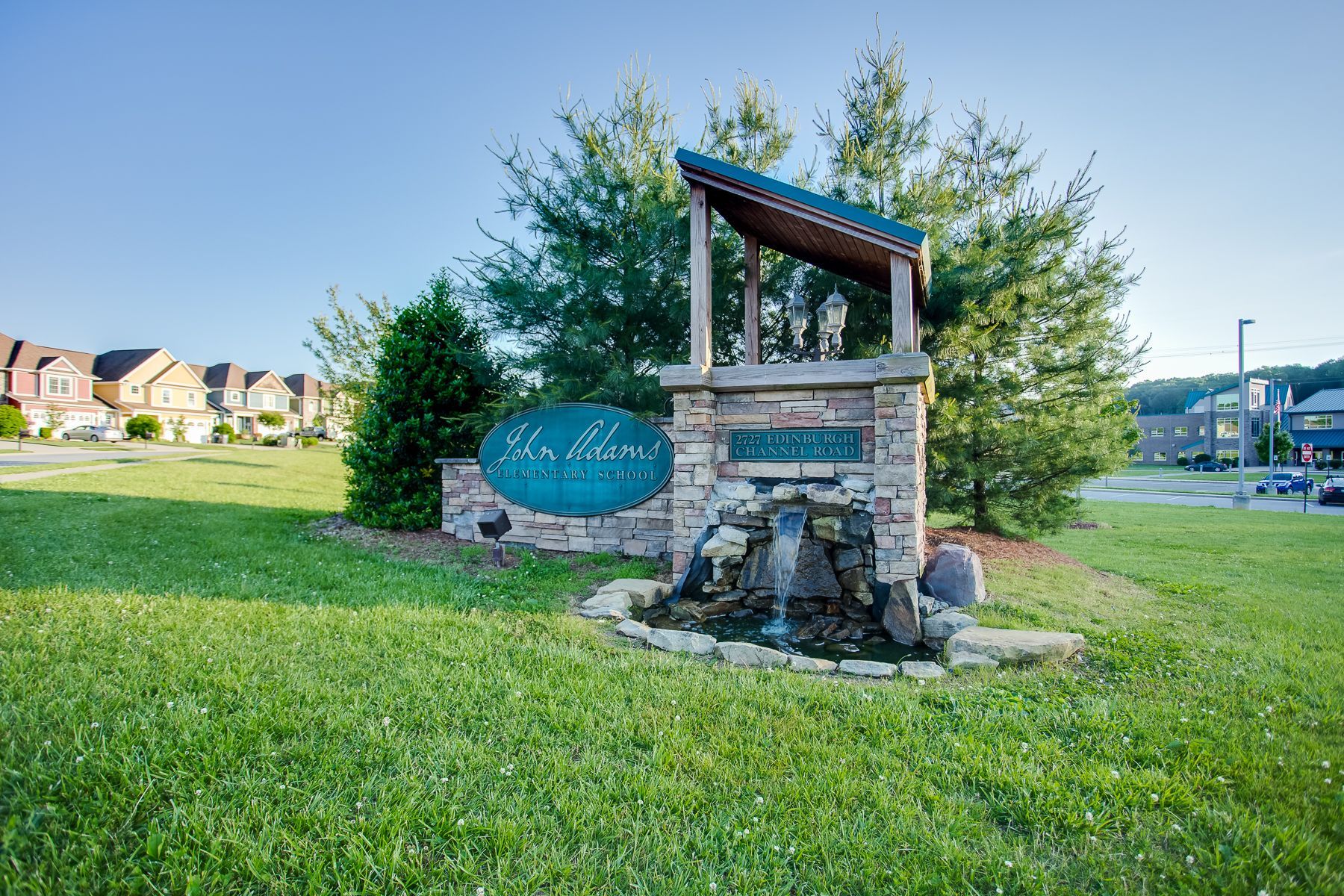A sign in the middle of a grassy field with a fountain in front of it.