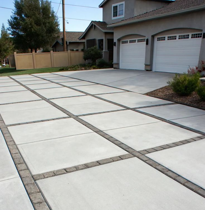 Concrete driveway with large square slabs and brick borders leading to a house with two garage doors.