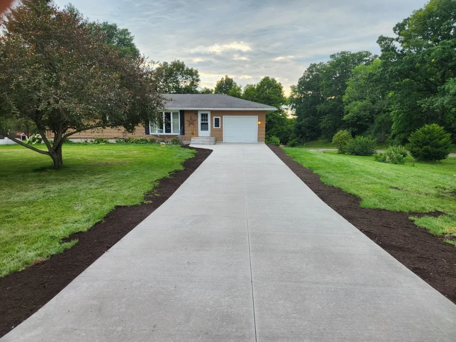 Single-story house with a long concrete driveway, green lawn, and trees on either side.