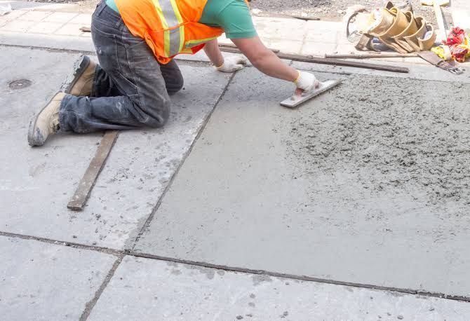 Construction worker smoothing wet concrete on a sidewalk with a trowel.