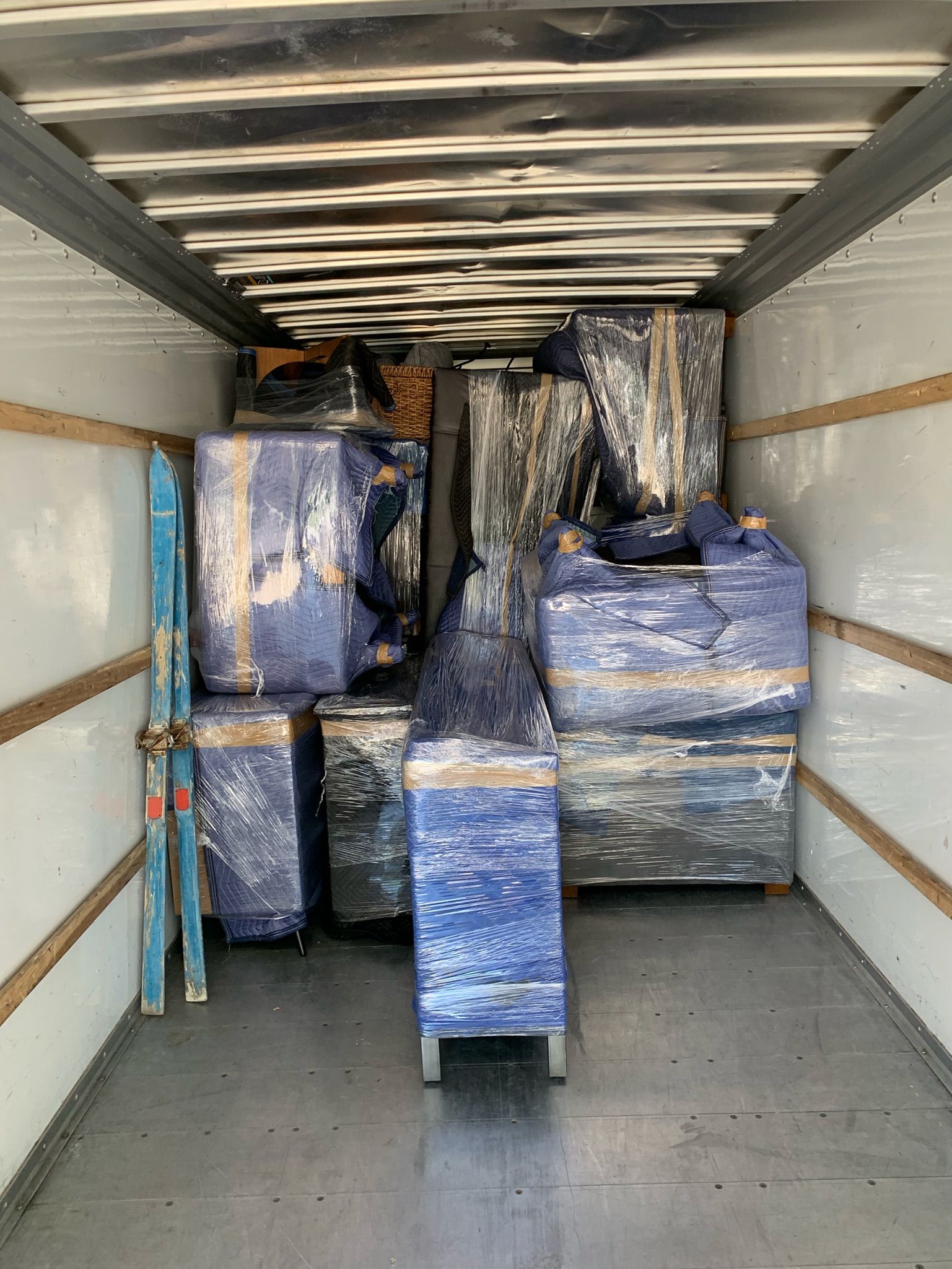 The inside of a moving truck filled with boxes wrapped in plastic.