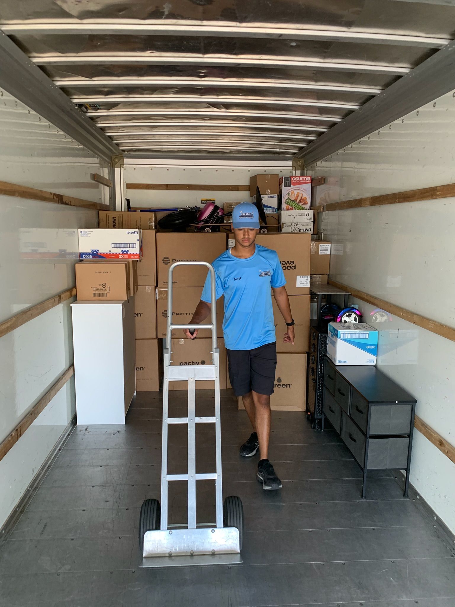 A man is pushing a dolly in a truck filled with boxes.