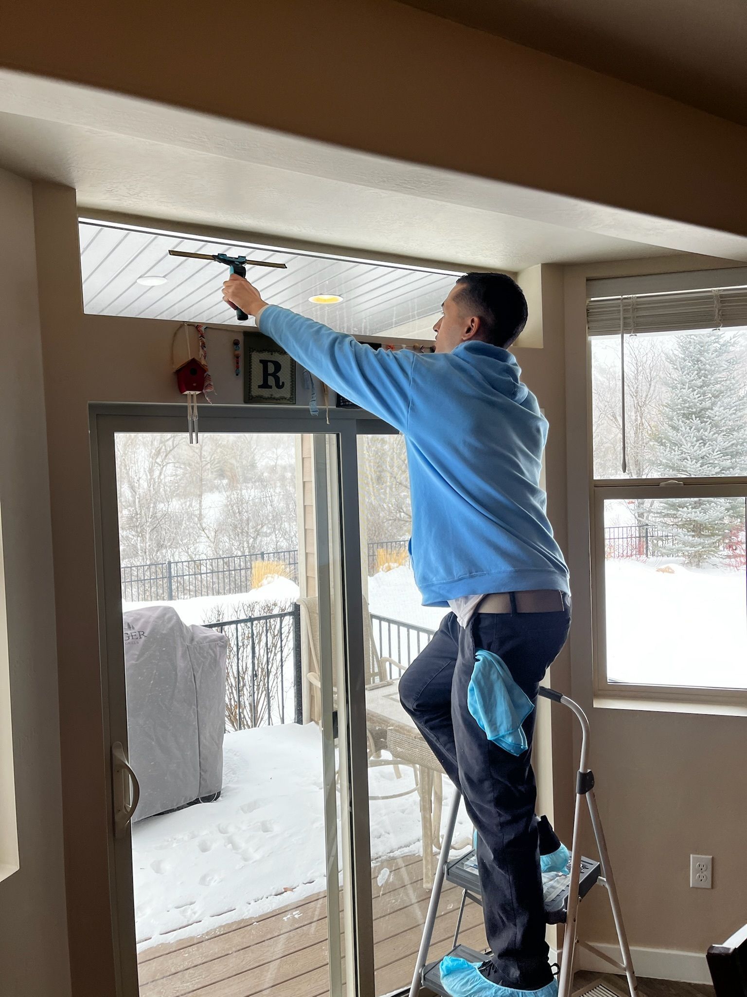 A man is cleaning a sliding glass door with a squeegee in a living room.