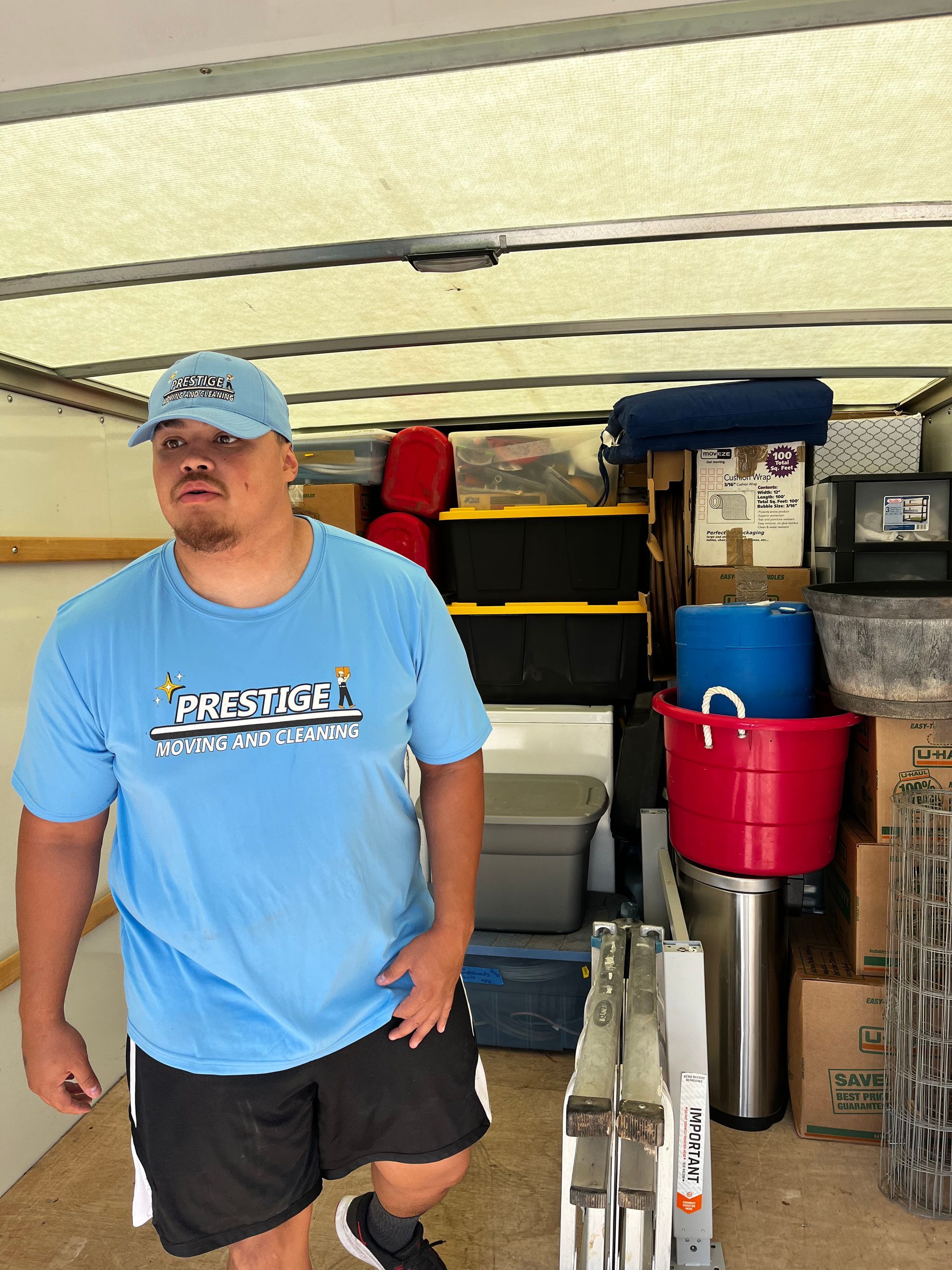 A man in a blue shirt is standing in the back of a moving truck.