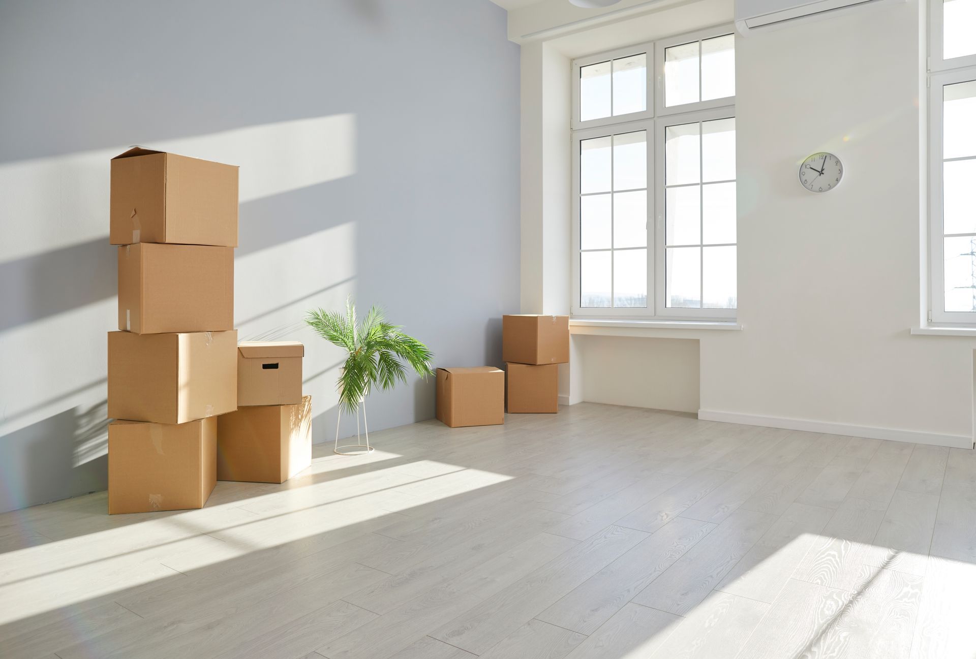 A stack of cardboard boxes in an empty room next to a window.