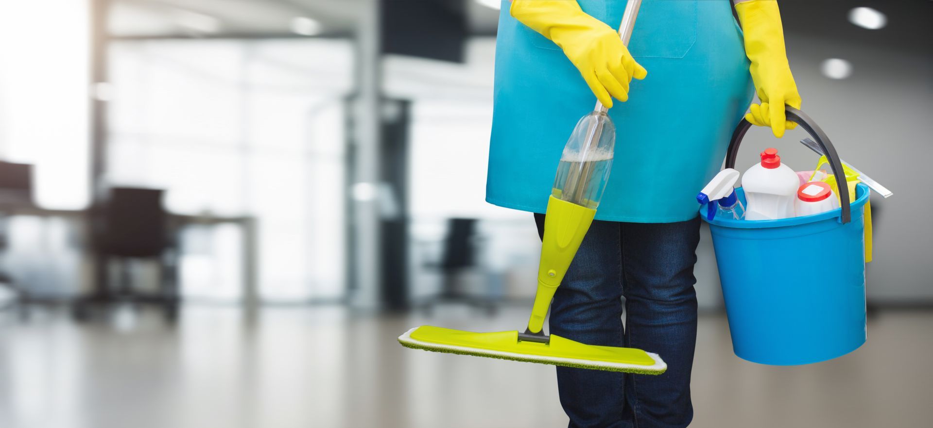 A woman is holding a mop and a bucket of cleaning supplies.
