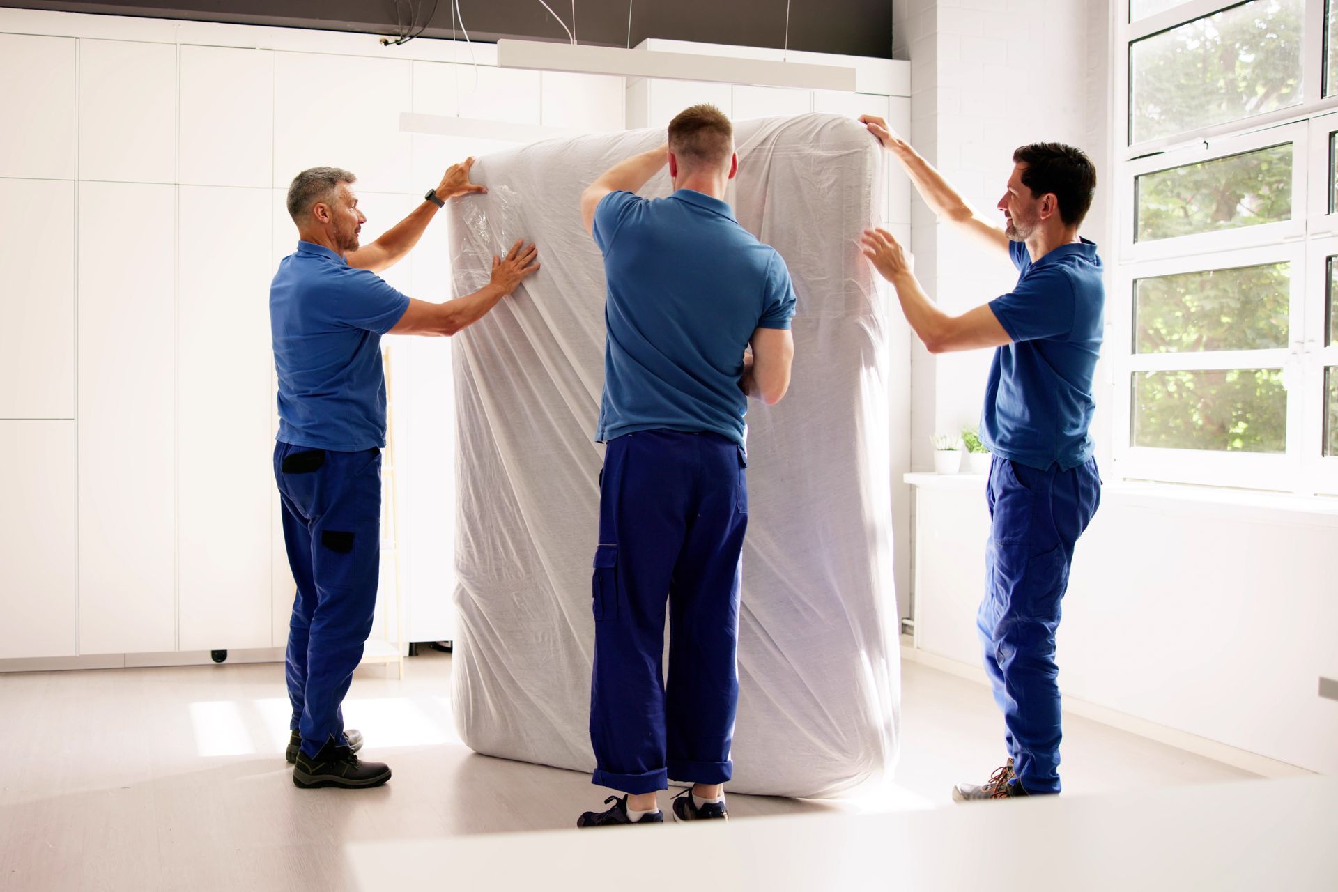 A group of men are wrapping a large white object in a room.