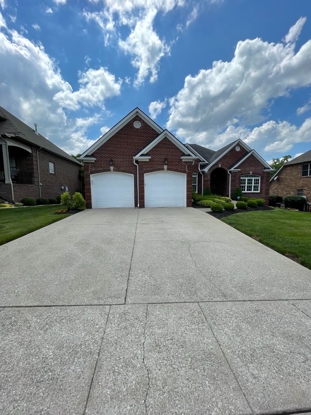 A brick house with two garage doors and a concrete driveway in front of it.
