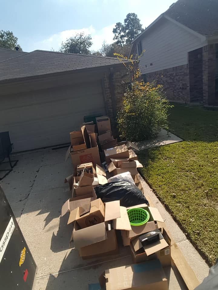 Boxes and assorted items stacked along a driveway beside a garage and lawn