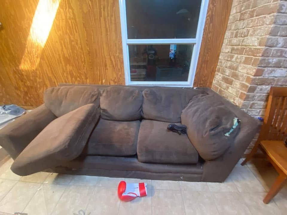 Brown couch against wood-paneled wall with window, a small red toy on the floor, and a chair beside it.