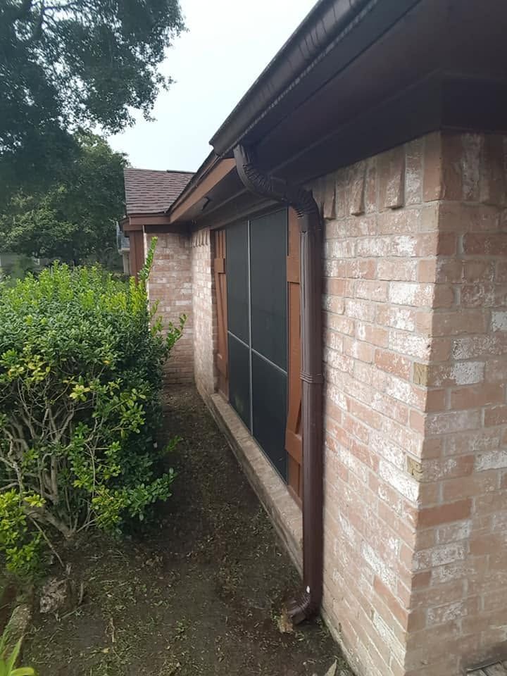 Brick house side wall with a screened door, narrow path, and greenery beside it